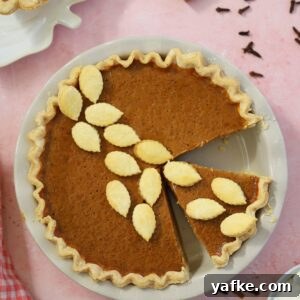 A gluten free pumpkin pie on a pink backdrop with cinnamon sticks and cloves surrounding it.