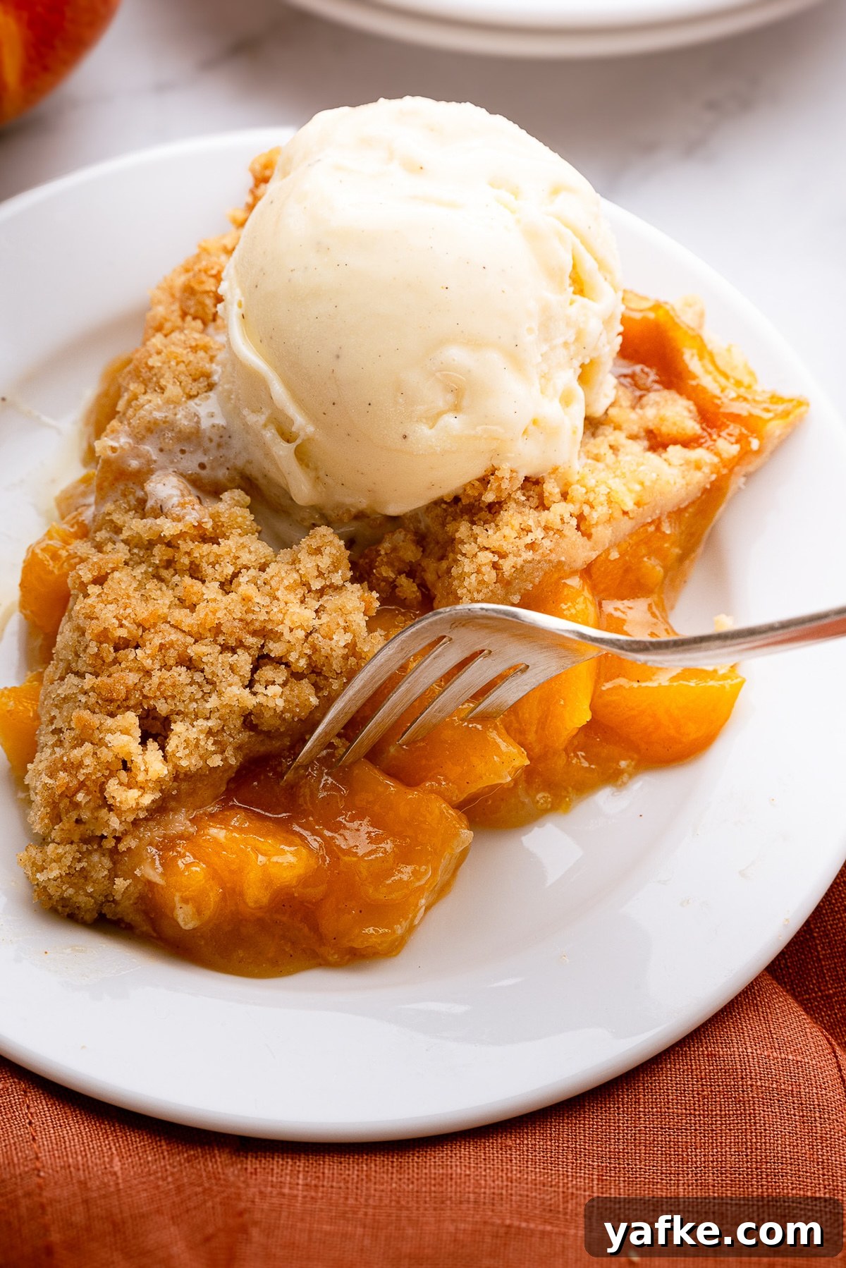 Classic Peach Crumble Pie with Brown Sugar Streusel 13 A slice of warm deep-dish peach pie topped with a melting scoop of vanilla ice cream on a rustic dessert plate.