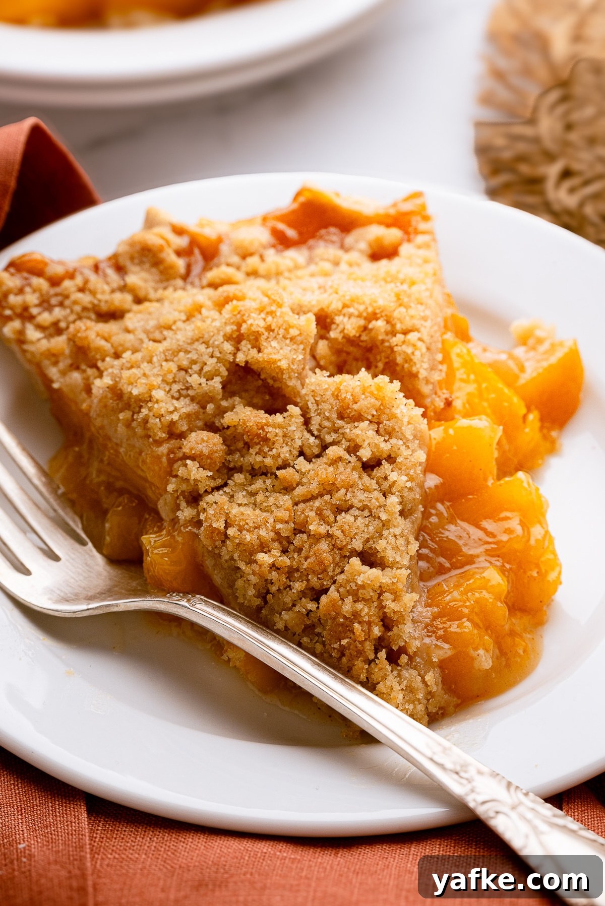 Classic Peach Crumble Pie with Brown Sugar Streusel 3 A clean slice of the best peach crumble pie on a small white dessert plate, showing the thick layers of velvety peach filling and crisp topping.