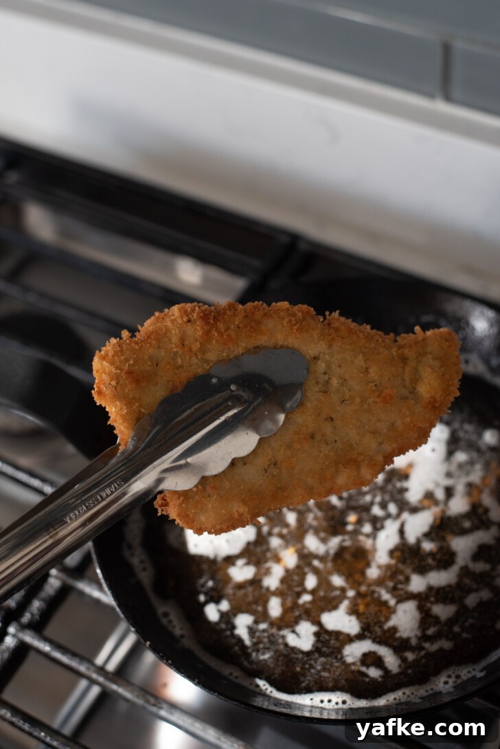 How to Make Crispy Japanese Tonkatsu in 30 Minutes 12 Tongs lifting a golden fried pork cutlet from hot oil