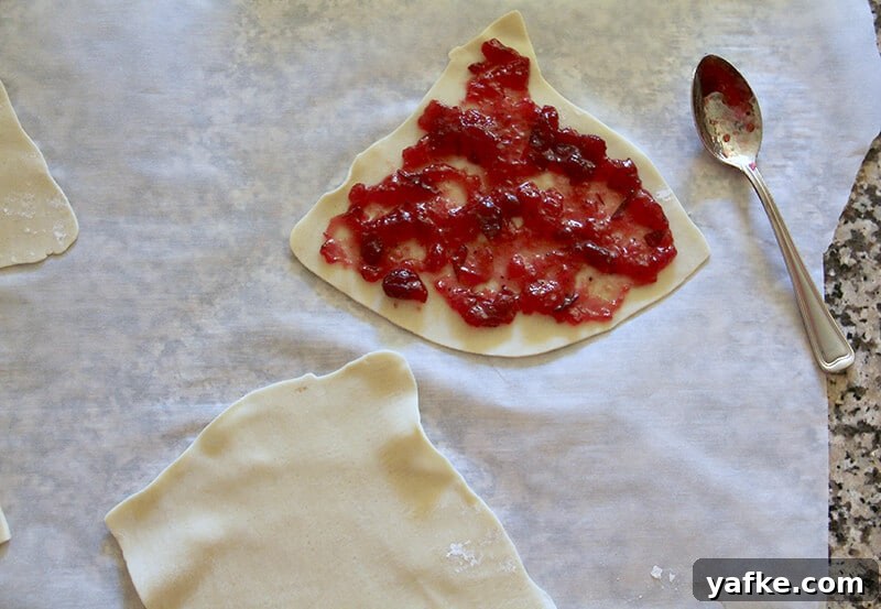 Turn Leftover Turkey into Cranberry and Boursin Hand Pies 2 Overhead shot of cranberry sauce on pie dough with a spoon beside it.