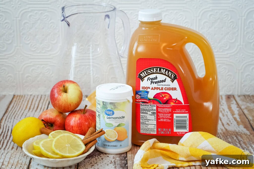 Sparkling Lemonade Cider Recipe 3 A large, glass pitcher, three red apples, a lemon, lemon slices, cinnamon sticks, Lemonade concentrate, and a gallon of apple cider.