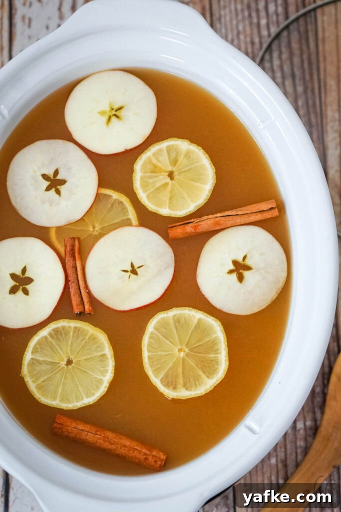 Sparkling Lemonade Cider Recipe 4 Lemonade Cider in a white crockpot with sliced apples, lemons and cinnamon sticks floating on top.