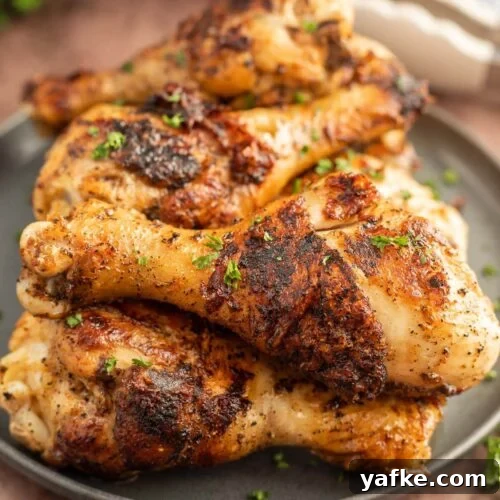 Low-Carb Chicken Recipes for Your Blackstone Griddle 10 A close-up of several seasoned and grilled Blackstone Drumsticks stacked on a dark plate, garnished with chopped fresh herbs.
