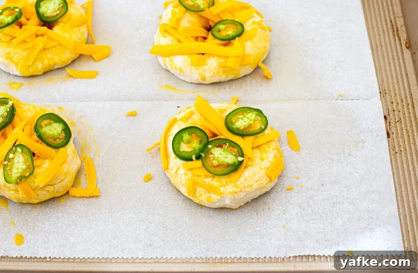Unbaked bagels topped with cheese and jalapeños.