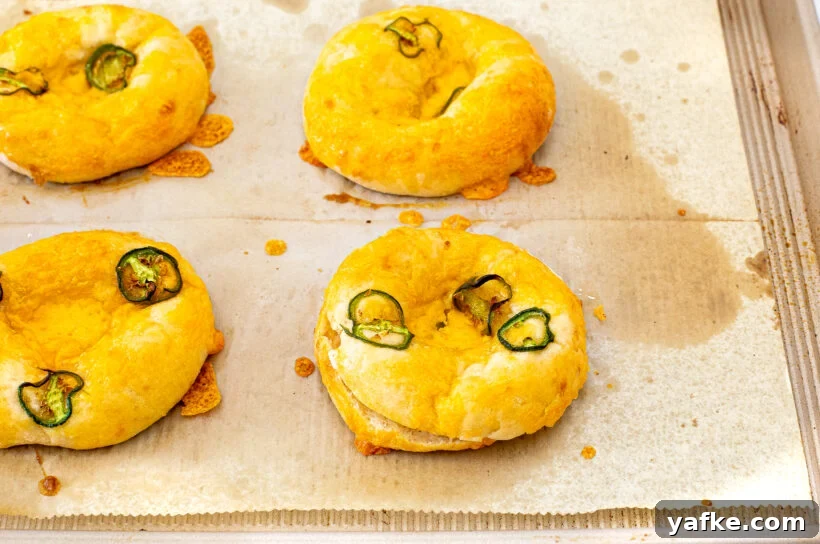 Four baked bagels topped with melted cheese and sliced jalapeños.