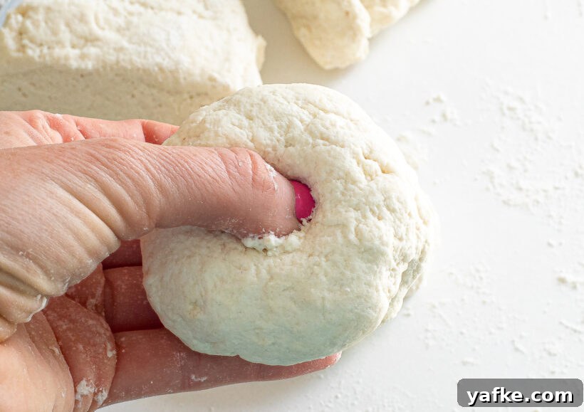 Finger poking a hole into the ball of bagel dough.