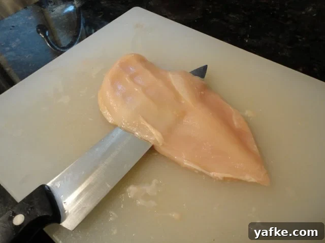 With the knife parallel to the cutting board, slice through the chicken breast with you other hand providing pressure